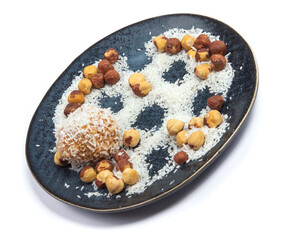 homemade coconut candies with almonds inside, sprinkled with coconut chips, lying on a round plate of dark blue color, decorated with hazelnuts isolate