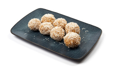 homemade coconut candies with almonds inside, sprinkled with coconut chips, lying on a rectangular plate of dark blue color, decorated with almonds on a white background