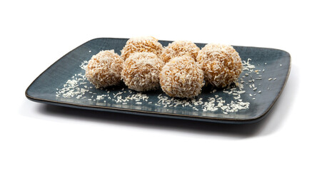 homemade coconut candies with almonds inside, sprinkled with coconut chips, lying on a rectangular plate of dark blue color, decorated with almonds on a white background