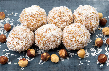 homemade coconut candies with almonds inside, sprinkled with coconut chips, lying on a rectangular plate of dark blue color, decorated with almonds on a white background