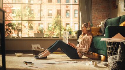 Young Girl Sitting on a Floor, Working or Studying on a Laptop. Female Freelancer Listening to Music and Typing on Keyboard. Cozy Living Room with Modern Interior and Creative Mess.