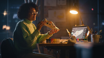 Active Black Female Designer Sitting in the Evening in Loft Studio and Working on Shoes Customisation. Living Room with Big Window. Next Generation and Trendy Fashion Design Concept.
