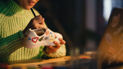 Close Up of Black Female Designer Putting Her Unique Drawing on Shoes, Working Late in the Evening in Loft Living Room. Millennial People and Fashion Trends in Clothing Design Concept.