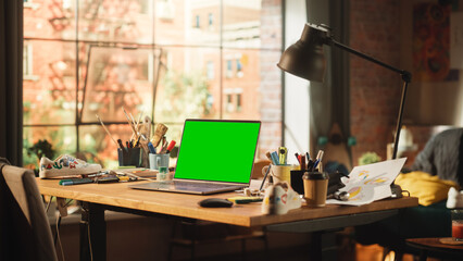 Laptop Computer with Mock Up Green Screen Chroma Key Display Standing on the Desk in the Modern Loft Workspace. Open Space Studio In the Background with City Window View.