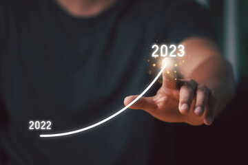 Man's hand pointing graph of success in 2023 year. The man plans to increase goal in 2023.