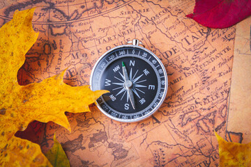 Fototapeta na wymiar Traveler's compass on map in bright multi-colored autumn leaves. Navigation in autumn.