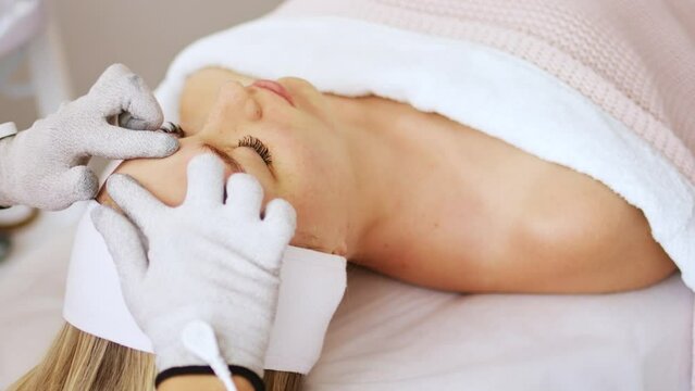 Beautician cosmetologist makes a procedure on the face with microcurrent therapy gloves. Hardware cosmetology in clinic salon for client.	