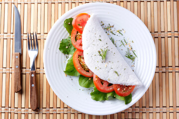 tapioca or beiju with vegetables, tomato, arugula, in white plate over rustic wooden table. Vegan,...