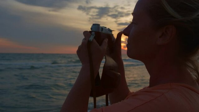 Inspired photographer takes pictures of beautiful landscape at sunset on retro film camera in travel.