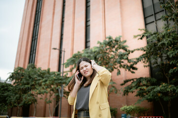 Young Asian woman using her phone to chat and send messages outdoors , Talking on the phone, headache with customers .Concept of business and communication