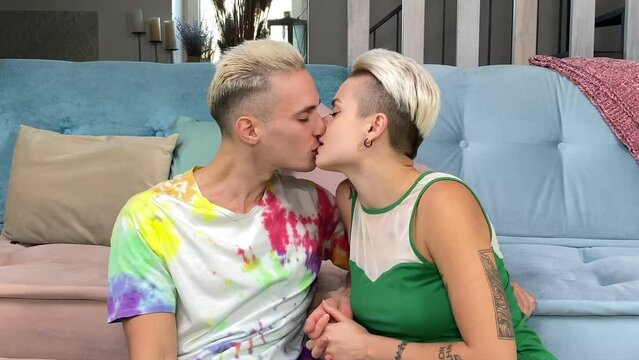 Stylish young couple kissing at home. Two affectionate young lovers sharing an intimate and passionate kiss together while sitting near couch indoors. Relationship, tenderness, bonding, love concept