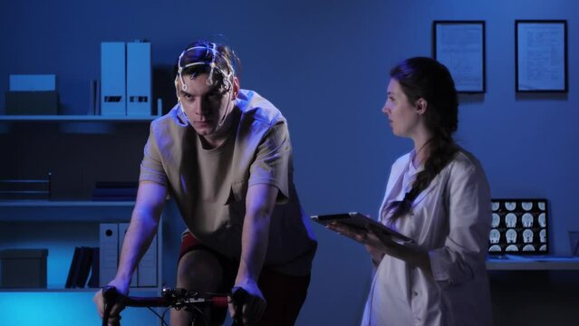 EEG topographer for examining brain, doctor making electrogram of scalp activity. Researching of brain work, man riding bicycle in electroencephalography headset. Rehabilitation after damage in sport.