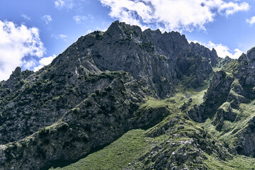 landscape of large steep rocky mountains next to a treeless grassy valley on a cloudy day, ruta del cares asturias, spain