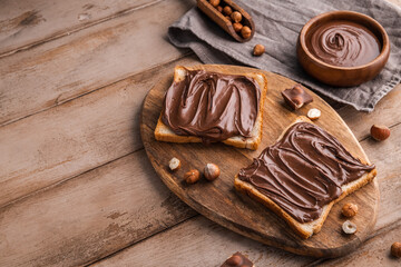Board of bread with chocolate paste and hazelnuts on wooden background