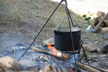 A saucepan on a tripod is hanging on the fire. Cooking while hiking in a tourist camp. Outdoor camping food. Space for text. An axe in the background.