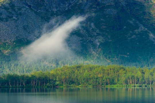 A cloud of fog over a flat smooth mountain lake