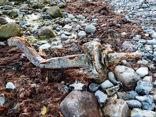 Rusty anchor on stony coast. Steel damaged by mechanical forces and salt water