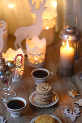 Two types of cookies, cups pf tea or coffee, various Christmas decorations and lit candles. Cozy Christmas atmosphere at home. Selective focus.
