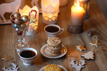 Fototapeta na wymiar Two types of cookies, cups pf tea or coffee, various Christmas decorations and lit candles. Cozy Christmas atmosphere at home. Selective focus.