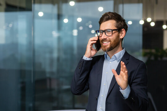 Mature businessman in a business suit talking on the phone, the manager is satisfied with the result of the achievement and work talks about the positive result, the man is at work inside the office.