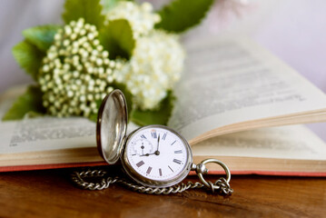 vintage old book with clock and flowers on wooden background	