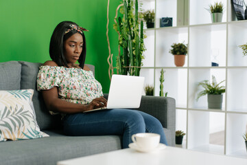Young african woman working on laptop computer at home sitting on sofa.