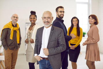 Multiracial diverse businesspeople pose together with old successful boss or director forefront. Smiling multiethnic employees or workers with senior leader in office. Business team, recruitment.