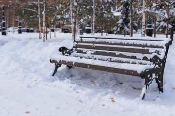 Winter wooden bench in park covered with snow - city and season concept
