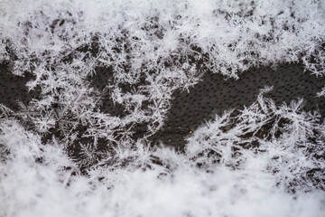 Macro image showing thousands of snowflake specimens. Snow covering a dark grey/black background with a window on middle right side of frame. 