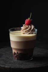 Layered dessert Trifles decorated with raspberry.  Sponge biscuit and three chocolate mousse layers. Chocolate souffle trifle cake in individual disposable transparent cups. Black background