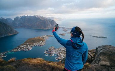 Woman taking photograph using a mobile phone during trekking. View from mountain on fjords and...