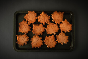 Gingerbread cookies with orange icing in the shape of fallen autumn leaves freshly baked out of the oven. Thanksgiving Day or Halloween festive background. Flat lay. Grey background