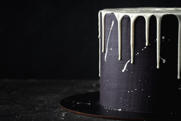 Black cake with white chocolate drips on the black background. Pouring chocolate on the cake. Chocolate drops on the cake