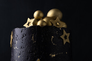 Luxury cake with dark blue cream cheese frosting decorated with golden chocolate stars and spheres. Birthday space themed cake on the black background