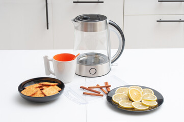 Tea drinking. Electric kettle, teacup, cookies, cinnamon and lemon on a kitchen table