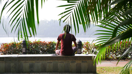 Old man sits quietly beside the lake in the morning and doing meditation.