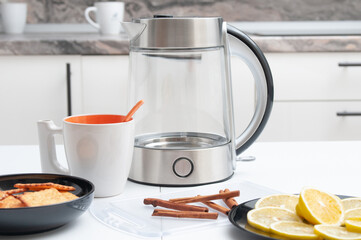 Tea drinking. Electric kettle, teacup, cookies, cinnamon and lemon on a kitchen table