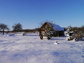 Scenic shot of a snow-covered field with a wooden house on a sunny day