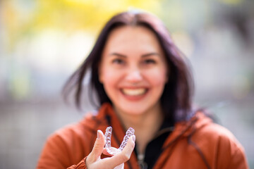 Happy young woman smiling with invisible teeth aligner during fall season at park.