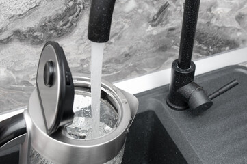 Obraz premium Pouring fresh clean water from a tap into an electric kettle