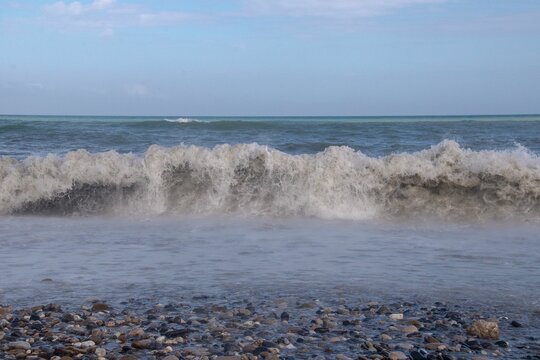 Sea waves splashing over the shore with a cloudy blue sky in the background