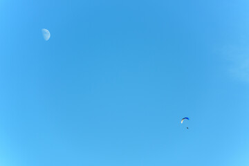 Paramotor in flight on a sunny day with the moon in the sky.