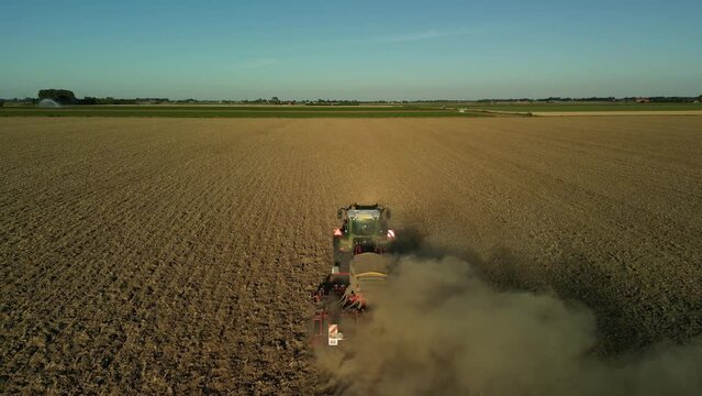 Drone shot of a tractor driving in the middle of a dry cultivated farm field leaving dust trails