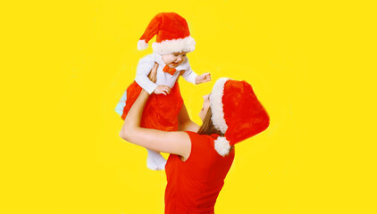 Fototapeta na wymiar Portrait of happy smiling mother and little child in christmas santa red hat on yellow background