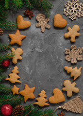 Christmas frame with traditional gingerbread cookies, fir branches and Christmas decoration on a grey background. Copy space.