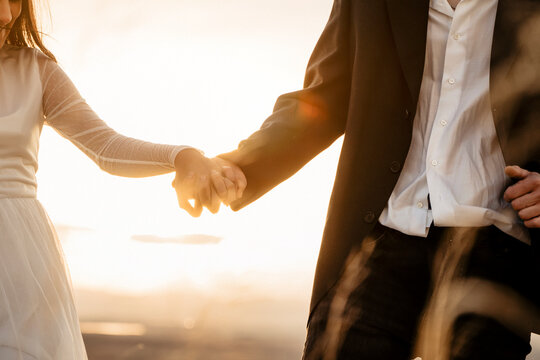 Pareja de recién casados dandose la mano en puesta de sol y mostrando las alianzas