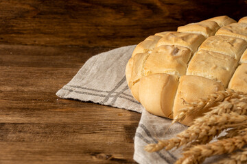 Close-up of ears of wheat and half a loaf of candeal bread on dark wooden table and background, selective focus, horizontal, with copy space