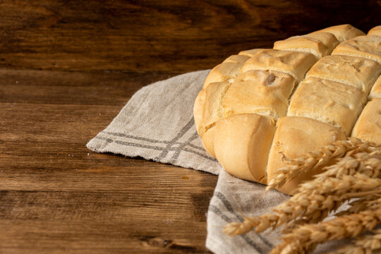 Close-up of ears of wheat and half a loaf of candeal bread on dark wooden table and background, selective focus, horizontal, with copy space