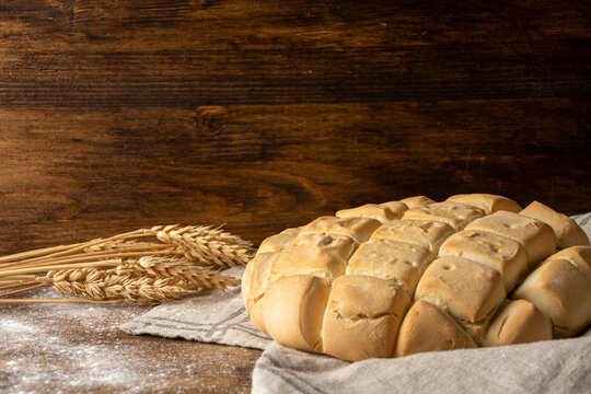 Top view of ears of wheat and loaf of white bread on kitchen towel and dark wooden table with flour, horizontal, with copy space