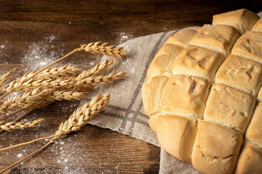 Top view of ears of wheat and half a loaf of candeal bread on kitchen cloth and dark wooden table with flour, horizontal